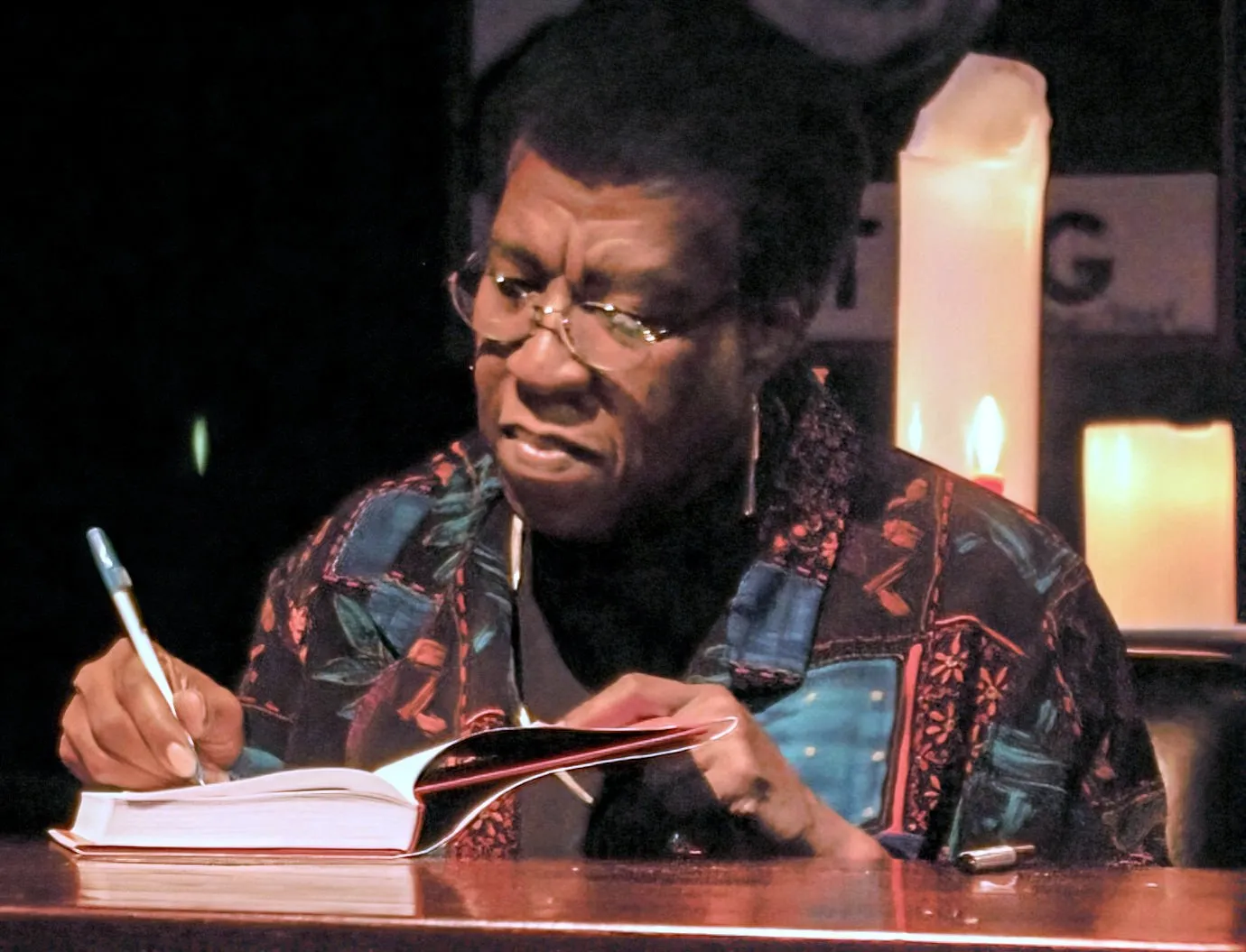 Octavia E. Butler at a book signing during the 2005 tour for Fledgling, pen in hand over an open book